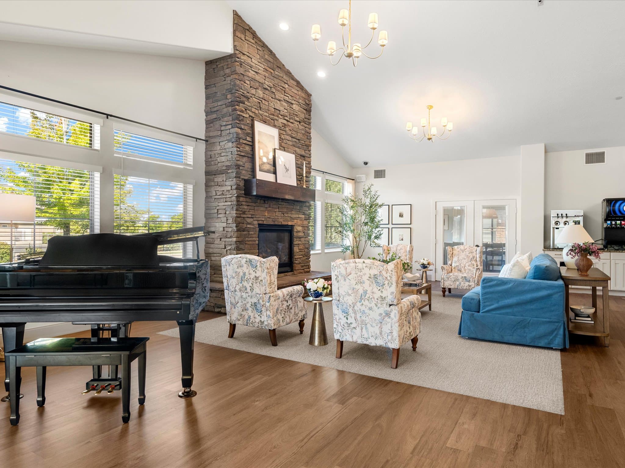 Great room with grand piano, stone fireplace, and floral wingback chairs