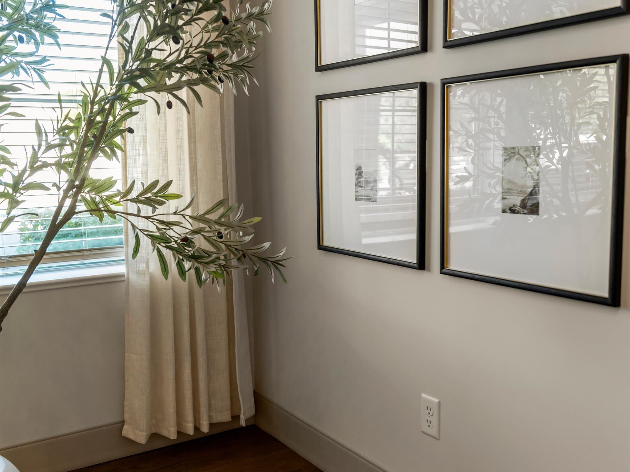 Framed gallery wall beside a window with sheer curtains and greenery
