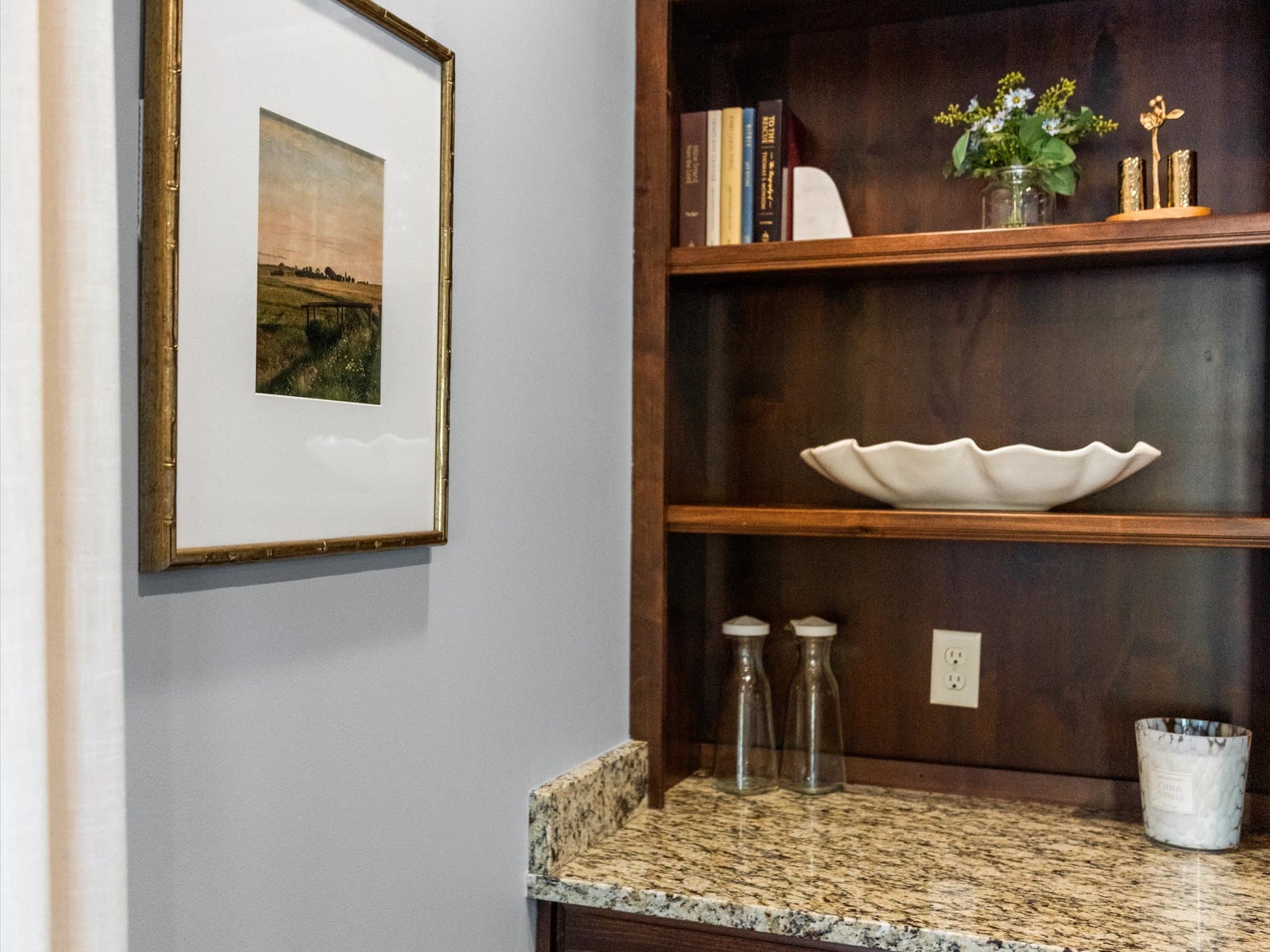 Framed landscape art beside built-in shelving with books and a ceramic bowl