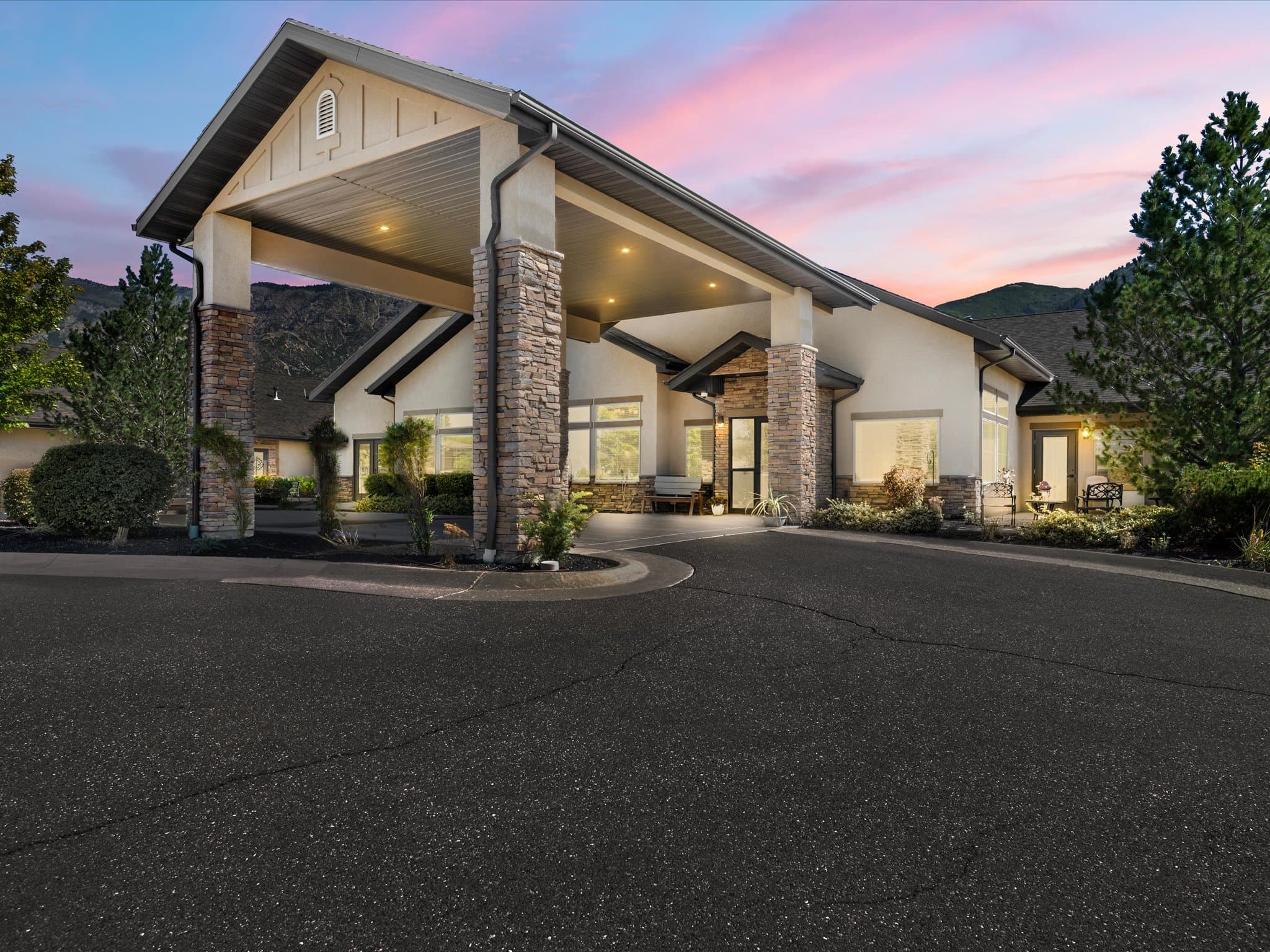 Covered entrance porte-cochère with stone columns at dusk, mountains behind