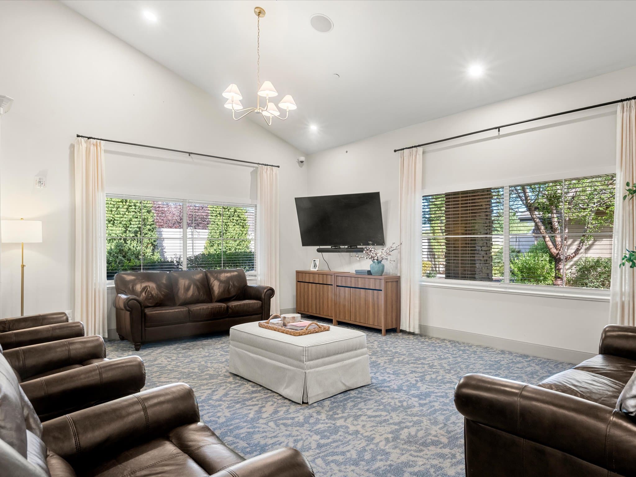 Memory care lounge with a leather sofa, TV, and garden views