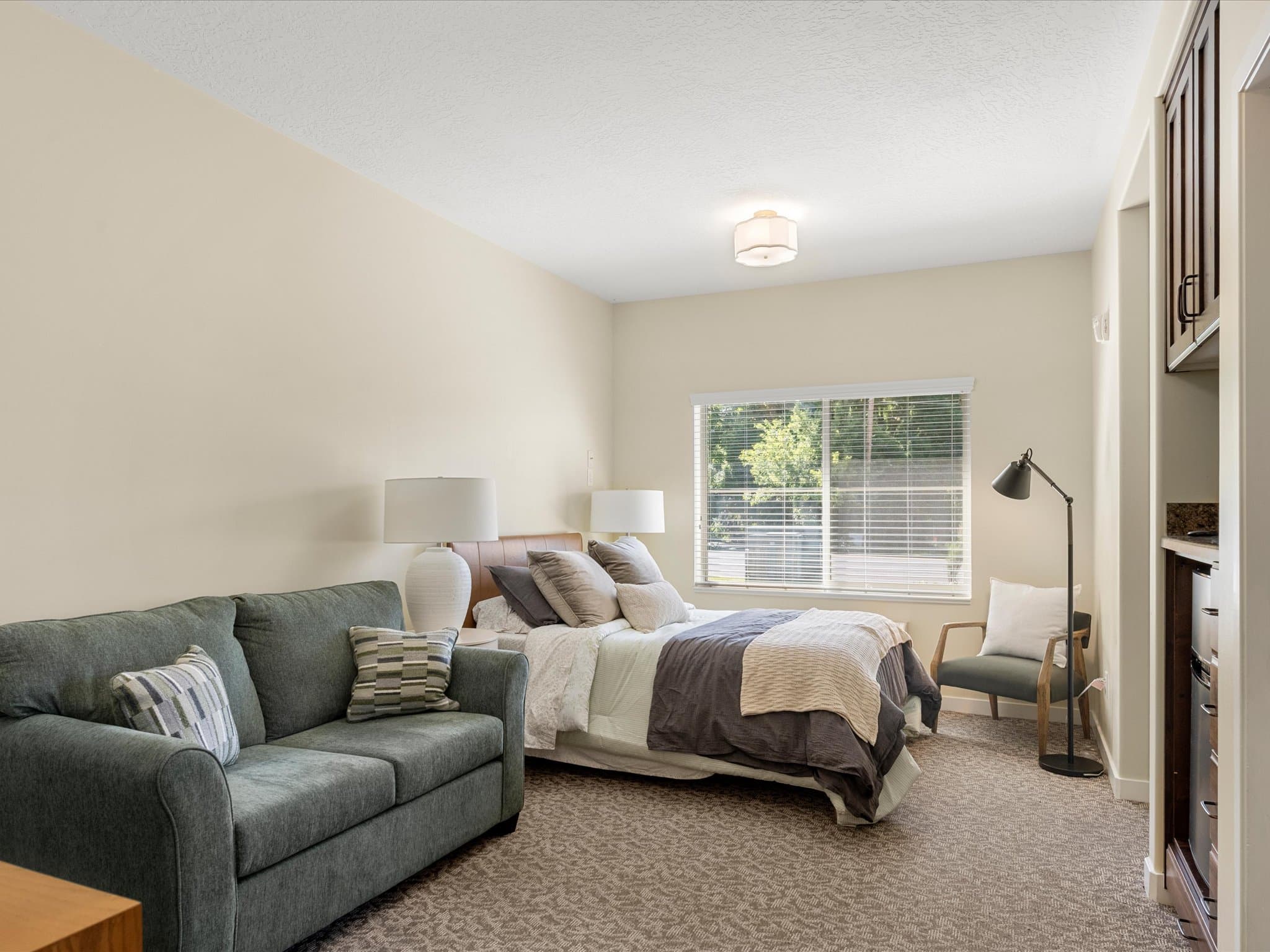 Model apartment with a queen bed, sofa, and large window