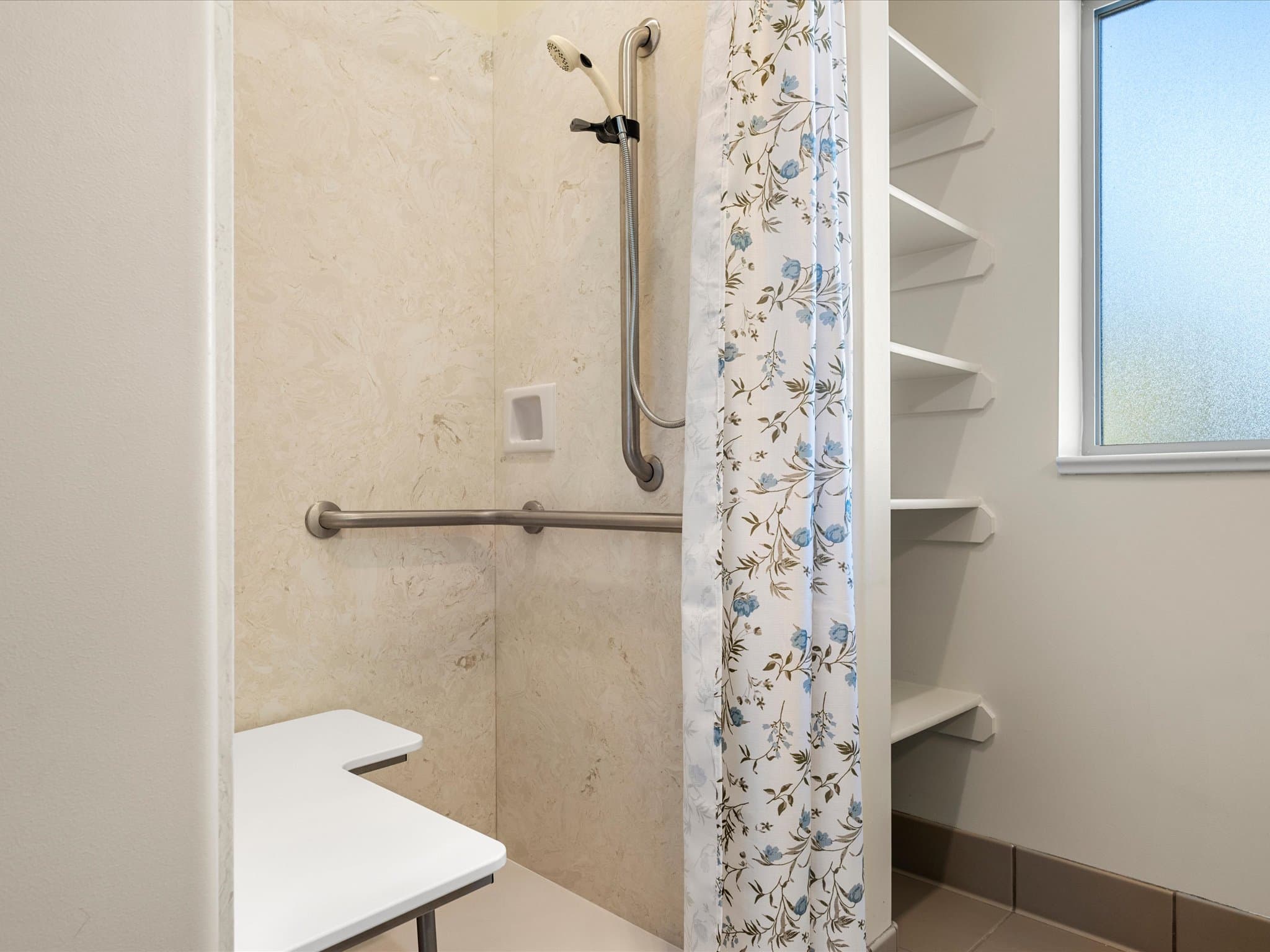 Curbless shower with grab bars and a fold-down bench in a model apartment bathroom